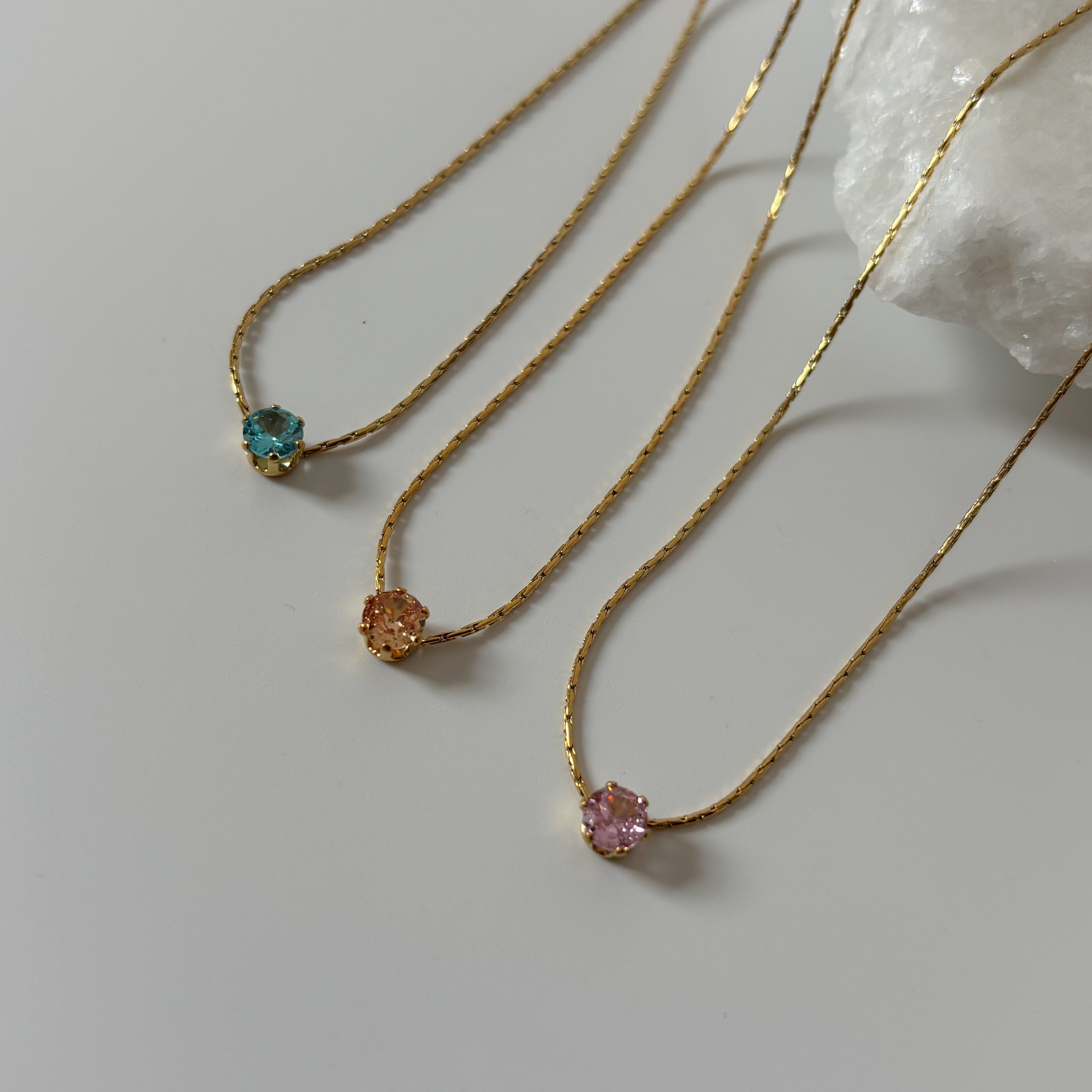 Three gold necklaces with gemstones on a light gray background