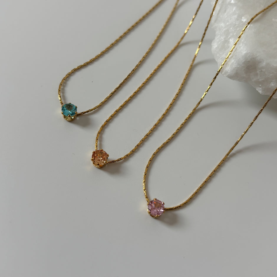 Three gold necklaces with gemstones on a light gray background