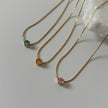 Three gold necklaces with gemstones on a light gray background